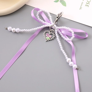 Détail du porte-clés à nœud en satin violet avec chaîne en perles et pendentif cœur