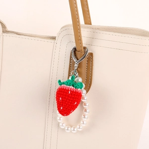 Handmade crochet strawberry keychain with pearls on tote bag, red yarn fruit charm