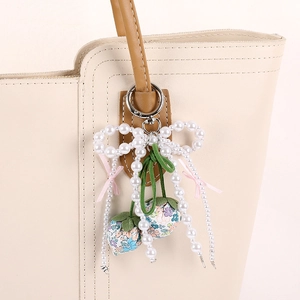 Floral strawberry pendant with pearl bow and satin ribbons on a beige leather tote bag