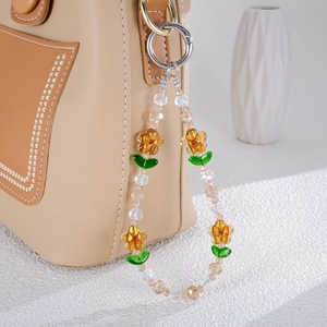 Detail of floral beaded phone strap with yellow petals and green leaves on a leather bag