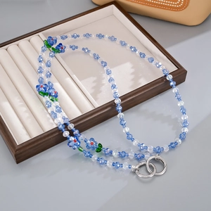 Blue and white floral beaded mobile strap with silver rings on a velvet tray