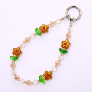 Handmade beaded phone strap with amber floral charms and green leaves on white background