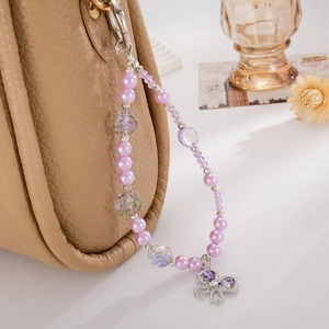 Elegant purple faux pearl phone charm with a silver butterfly pendant on a leather bag