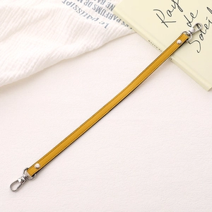 Detail of yellow PU leather bag strap with silver lobster clasps and metal rivets