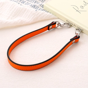 Close-up of orange leather bag strap with silver metal hooks on a white textured surface