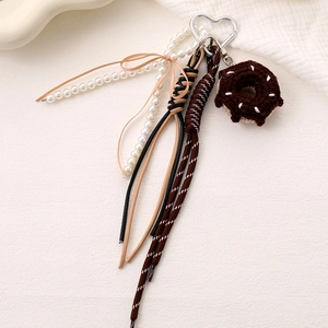 Detail of crochet donut bag charm with white pearls, brown bow, and heart-shaped silver clasp