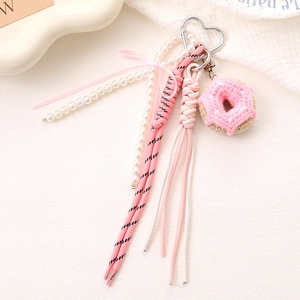 Pink handmade crochet donut phone charm with pearls and bow on a white textured background