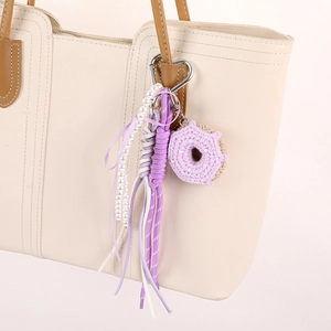 Handmade crochet donut phone charm with pearls and nylon cord on a cream tote bag