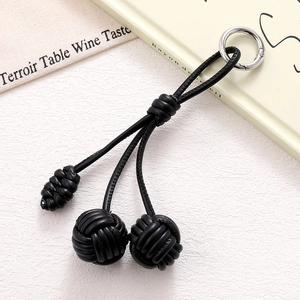 Detail of hand-woven black PU leather strap phone charm with triple sphere knots