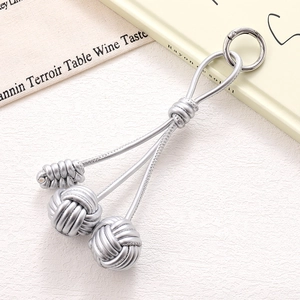 Close-up of metallic silver woven triple ball keychain with circular hook on white fabric