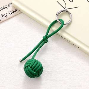 Detail of green woven ball keychain with PU leather strap and silver spring buckle