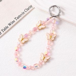 Pink crystal beaded phone strap with gold butterfly charm on a white textured base