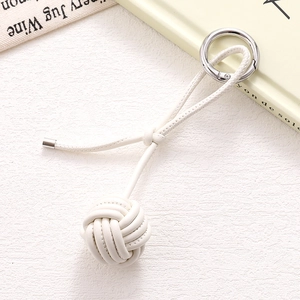 Handwoven cream PU leather ball keychain with polished silver ring on a white texture background