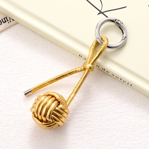 Macro detail of hand-woven gold knot charm with metallic finish and silver ring connector