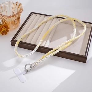 Detail view of woven yellow and white sequin phone strap with silver ring on wooden tray