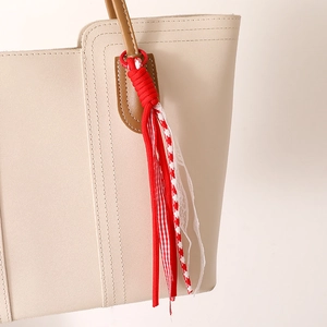 Bijou de sac en corde tressée rouge avec dentelle et rubans à carreaux sur sac beige