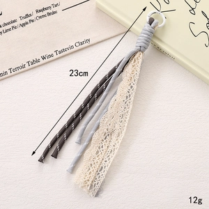 Détail d'un bijou de sac tressé de 23cm avec franges grises et rubans en dentelle