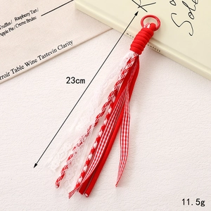 Détail d'un pendentif gland tissé rouge et blanc avec rubans dentelle et mesure de 23 cm