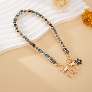 Detail of woven chain strap with gold metal, red plaid fabric and black enamel flower