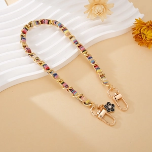 Detail of woven chain strap with golden clasps and a black camellia flower charm