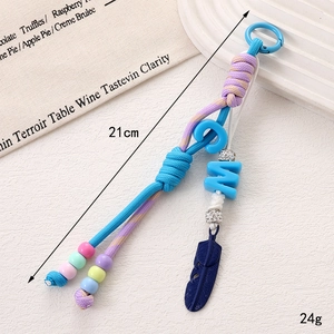 Détail du bijou de sac en nylon avec perles colorées, plume en métal et fermoir cristal
