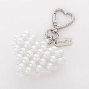 Close-up of heart-shaped pearl bag charm with silver Good Luck metal tag and hook