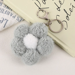 Close-up of soft grey plush flower keychain with silver metal clasp on warm aesthetic background