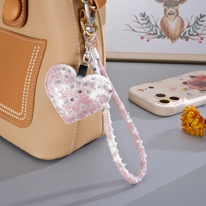 Close-up of pink tweed heart bag charm with sequins and metallic hook on a beige purse