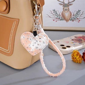 Pink heart-shaped denim charm with silver sequins hanging on a beige handbag