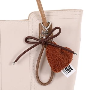 Brown plush heart bag charm with dark bow and silver metal clasp on cream leather bag