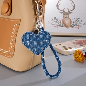 Detail of blue denim heart charm with silver sequins hanging on a stylish beige handbag