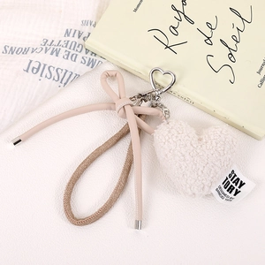 Detail view of plush beige heart bag charm with leather bow and silver metal clasp