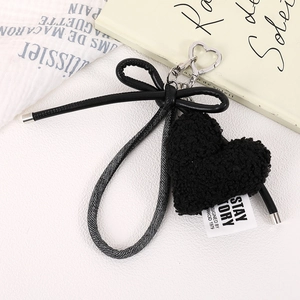 Detailed view of black plush heart charm with a leather bow and silver metal clasp