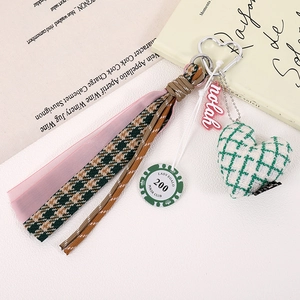 Macro detail of houndstooth fabric heart pendant and green poker chip on a metal clip