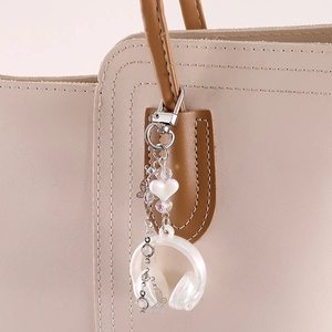 Pearlescent earphone bag charm with heart bead and hollow butterfly on a beige bag