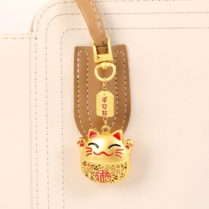 Golden alloy lucky cat bag charm with safety talisman on beige leather handbag