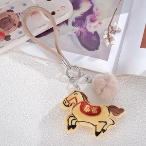 Detail of embroidered horse charm with golden lucky text and soft plush pom pom