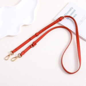 Macro detail of orange pebble leather strap with golden metal lobster clasps and stitching