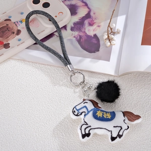 Detail of embroidered horse plush charm with lucky text, black pompom and metal clasp