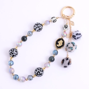 Leopard print bead phone strap with fuzzy pom-poms and gold spring clasp on white backdrop