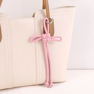 Pink PU leather woven knot bag charm with silver metal ring on off-white handbag