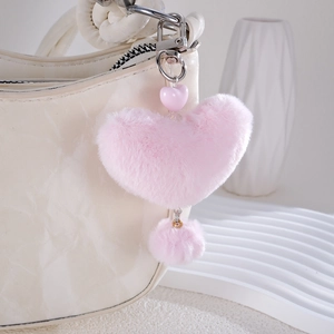 Pink heart-shaped plush keychain with acrylic beads and faux fur ball on a white bag