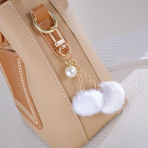 Detail of faux leather bag with golden chain charm featuring white pearls and soft pom-poms