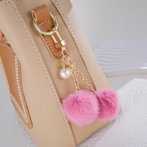 Pink plush ball bag charm with pearl pendant on beige leather bag accessories