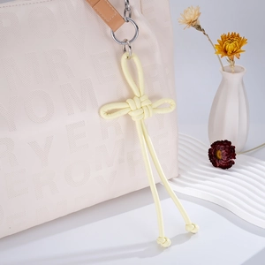 Detail of a handmade light yellow woven leather Chinese knot charm on a beige handbag