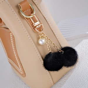 Close-up of fluffy black pompom bag charm with white pearl and gold metal hardware
