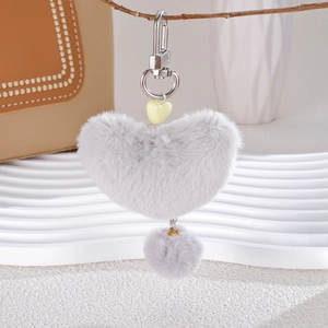 Close-up of grey plush heart keychain accessory with silver metal clasp on a leather bag