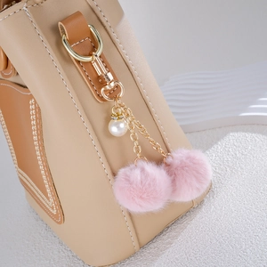 Close-up of pink faux fur double ball charm with pearl on beige leather handbag detail