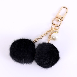 Creative double fur ball keychain with pearl pendant and gold chain on white background