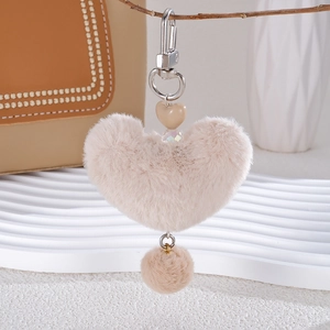 Detail of plush beige heart bag charm on a wooden branch with aesthetic decor